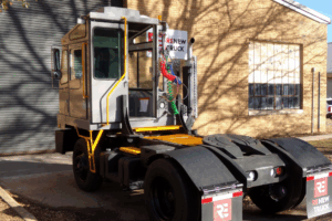 Yard Truck Fleet in New Boston, TX by Renew Truck. A gray yard truck with a boxy cab and “Renew Truck” mudflaps parked outside a brick building.