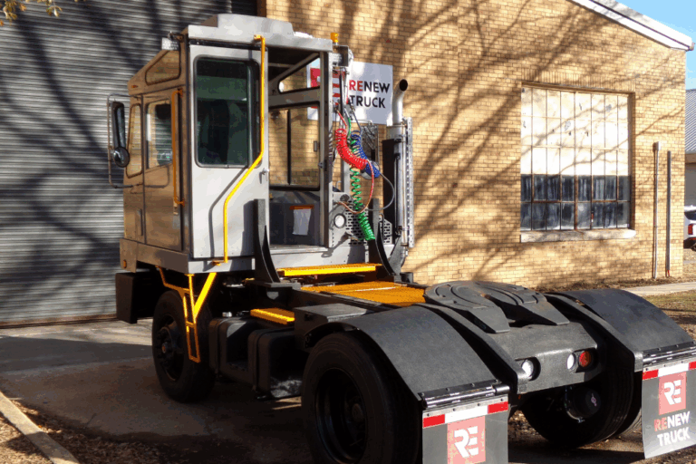 Yard Truck Fleet in New Boston, TX by Renew Truck. A gray yard truck with a boxy cab and “Renew Truck” mudflaps parked outside a brick building.