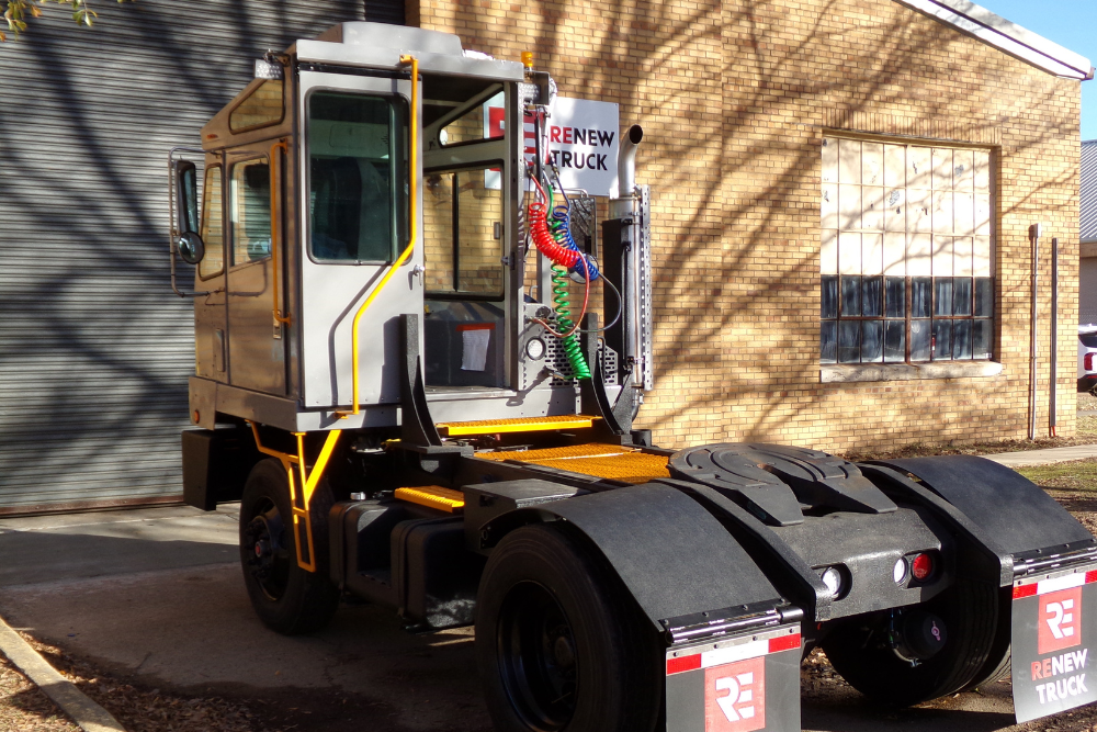 Yard Truck Fleet in New Boston, TX by Renew Truck. A gray yard truck with a boxy cab and “Renew Truck” mudflaps parked outside a brick building.